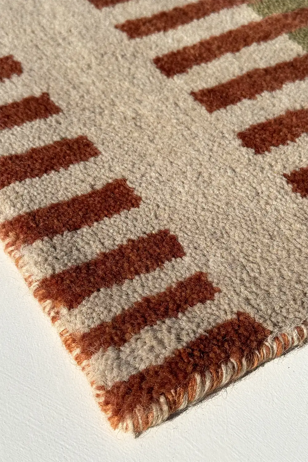 Close-up of a multicolor striped long runner rug with burnt orange and beige colors on a white floor.