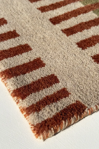 Close-up of a multicolor striped long runner rug with burnt orange and beige colors on a white floor.