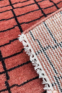 Close-up of a textured rust rug with a grid pattern and white fringe.
