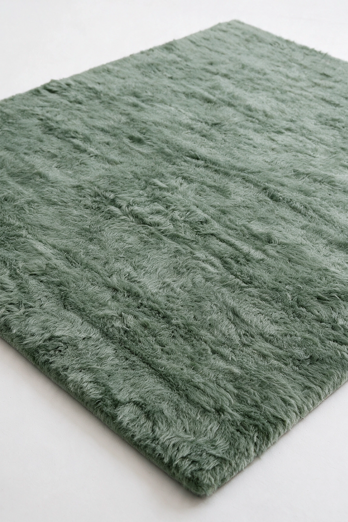 A sage green shaggy area rug shown at an angle on a plain white background.