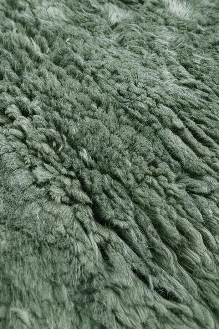 A close-up of a shaggy, long-pile rug in a muted sage green color, showing the soft texture and dense fibers.