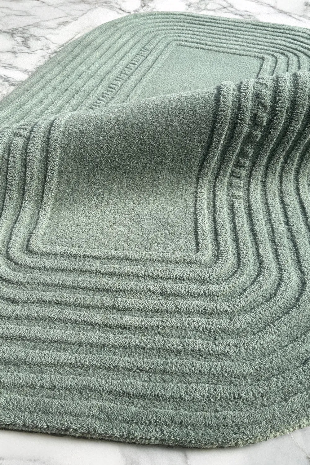 soft sage green textured wool rug on a marble surface