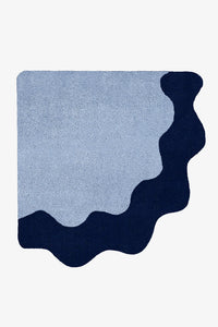 An abstract area rug with a wavy organic silhouette, featuring a light blue center and a dark navy bottom and right border, shown on a plain white background.
