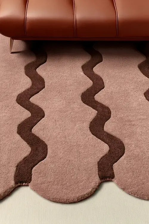 Close-up of a neutral rug with wavy brown border next to a brown leather chair.