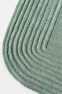Close-up of oval corner showing layered carved lines in sage green wool, ideal for green room decor or eco-friendly homes