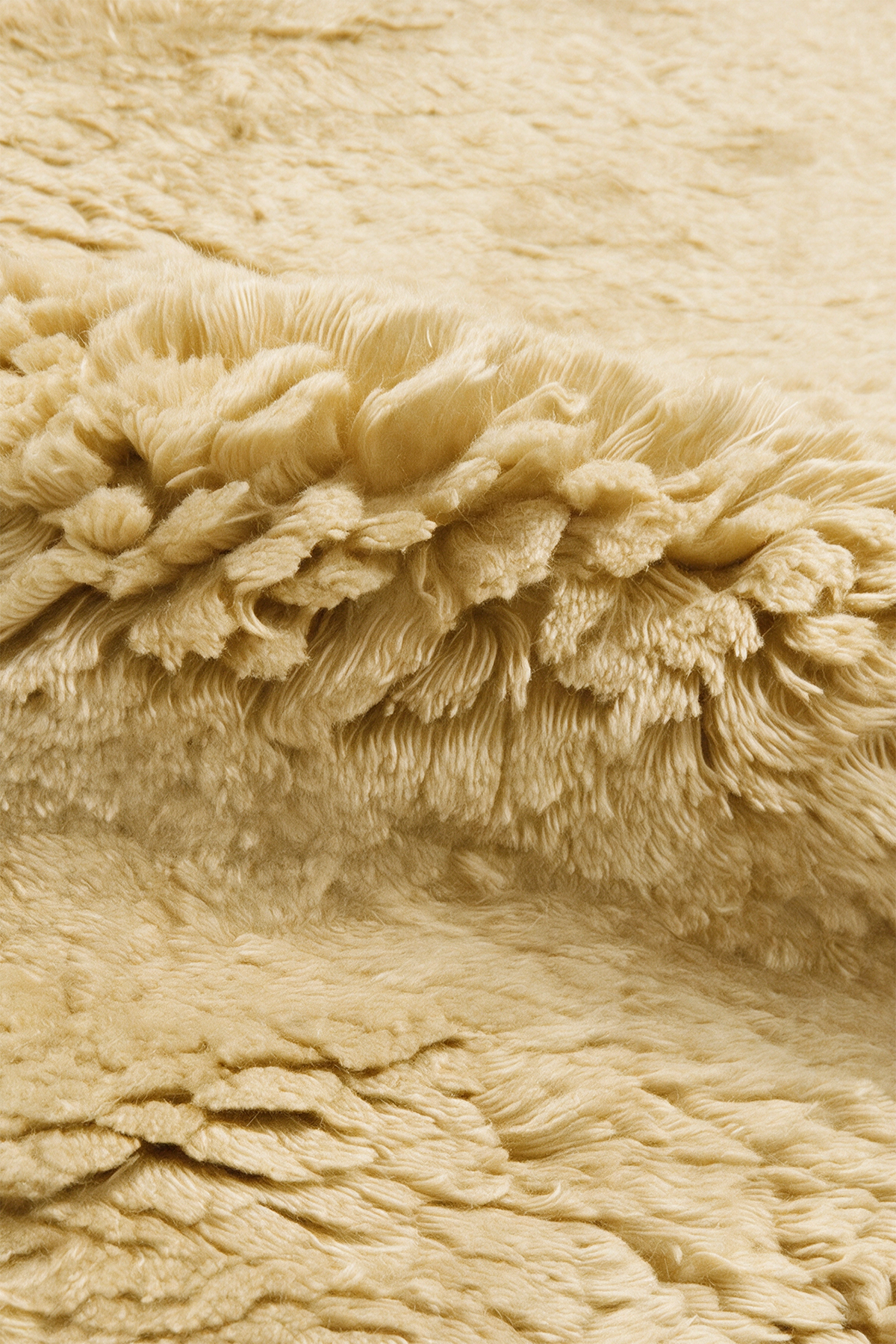 Close-up of a plush, shaggy yellow rug with a ruffled, textured surface.
