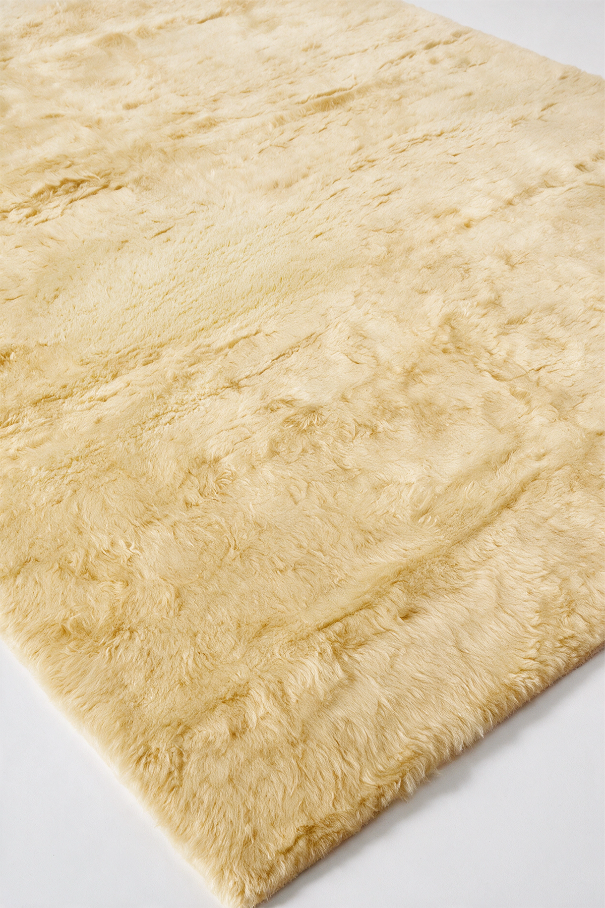 A close-up of a soft, fluffy area rug in a light yellow, showing the texture of the pile from an elevated angle.