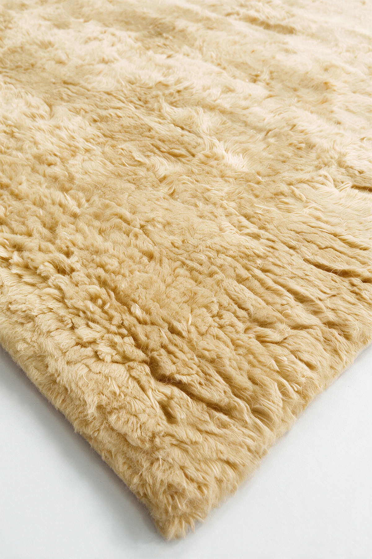 A close-up of a fluffy, shaggy area rug in a soft yellow, showing the texture of the pile against a plain white background.