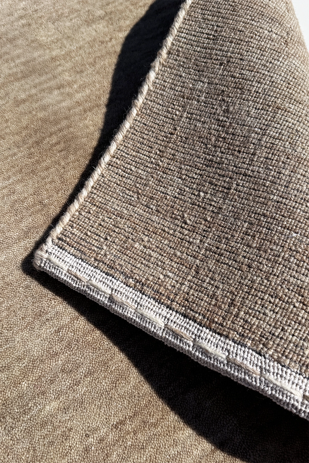 Close-up of a neutral runner rug showing a taupe-brown pile with a contrasting light beige stitched edge stone texture 