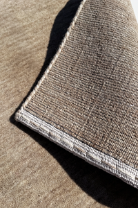 Close-up of a neutral runner rug showing a taupe-brown pile with a contrasting light beige stitched edge stone texture 