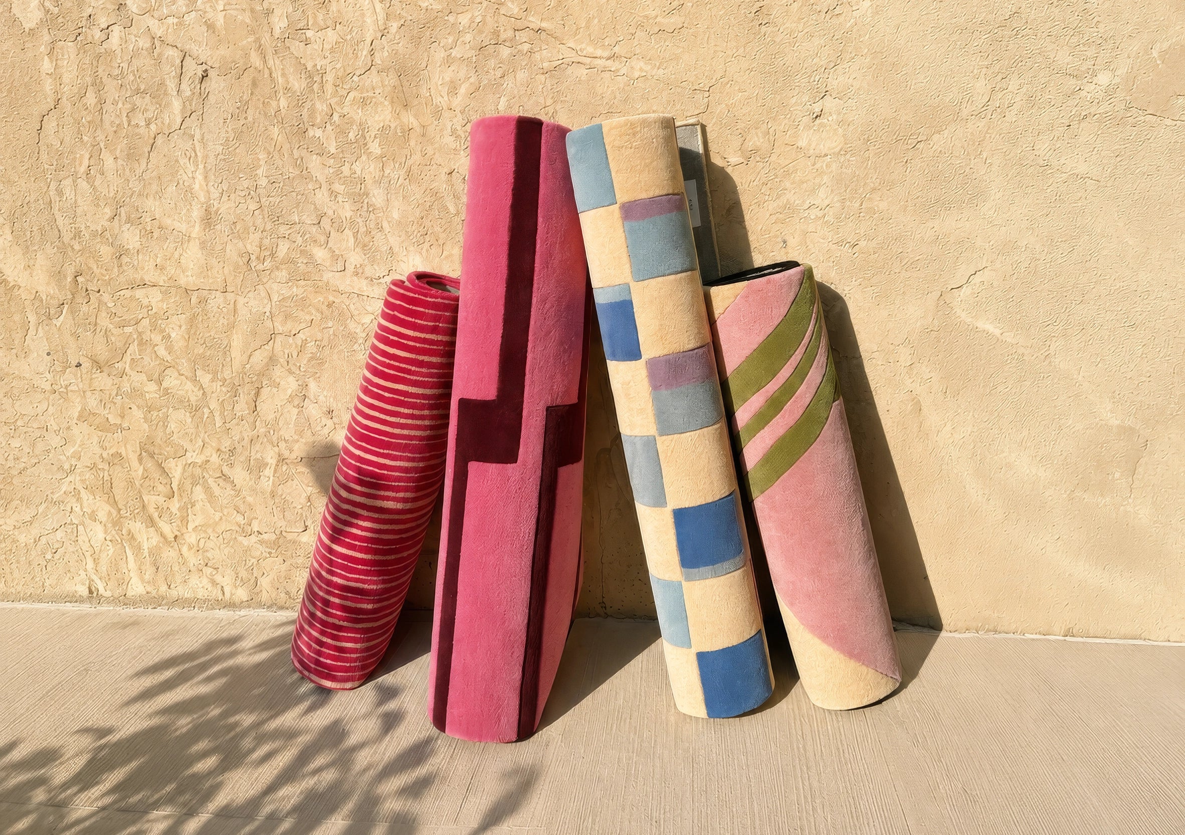 Four colorful rugs stacked against a beige wall