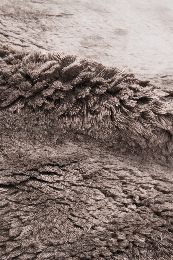 Close-up of a shaggy wool rug taupe-brown color, showing the dense textured pile and folded fibers.