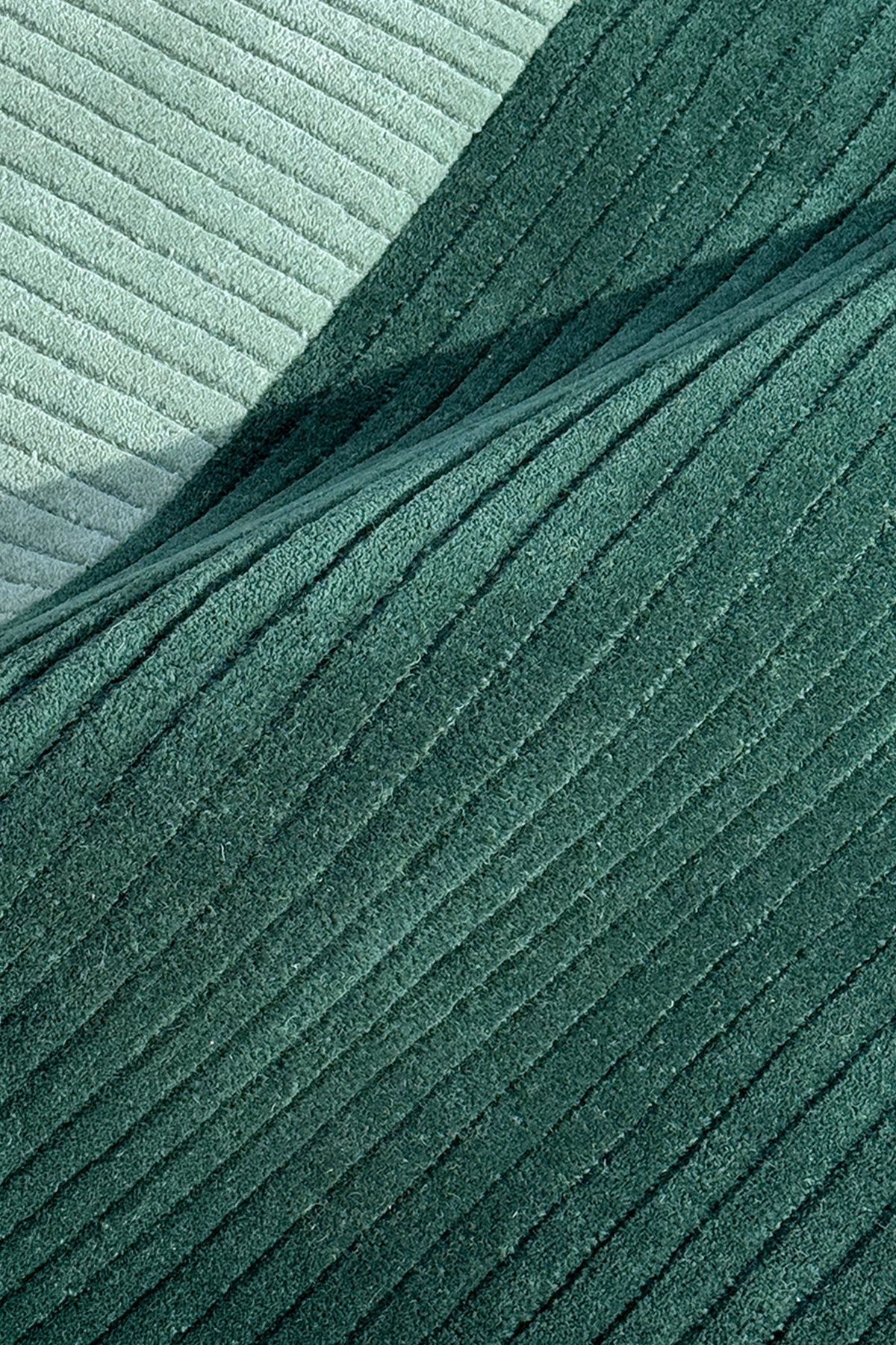 A close-up of ribbed rug in two shades of green, with a darker forest green fold layered over a lighter sage green background teal