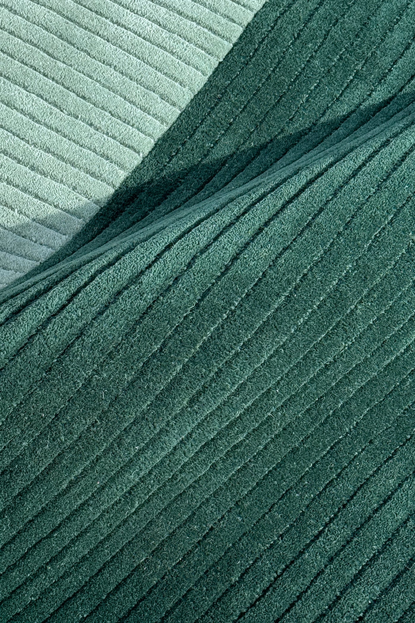 A close-up of ribbed rug in two shades of green, with a darker forest green fold layered over a lighter sage green background teal