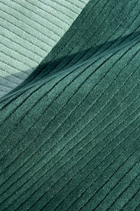 A close-up of ribbed rug in two shades of green, with a darker forest green fold layered over a lighter sage green background teal