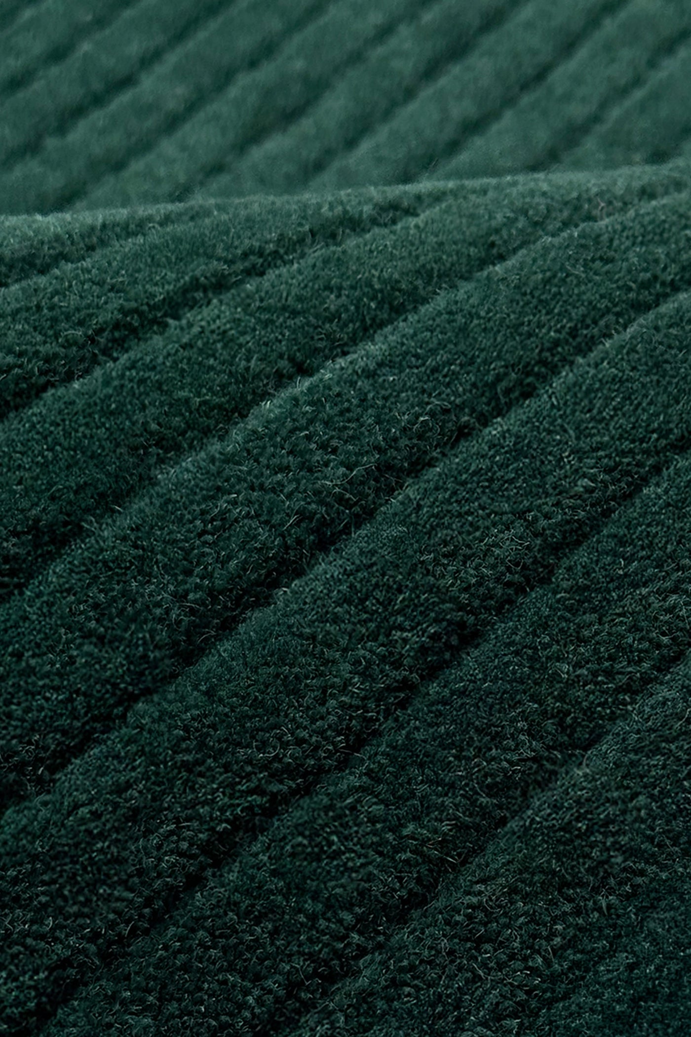 A close-up of dark green ribbed rug texture with diagonal stitched stripes teal