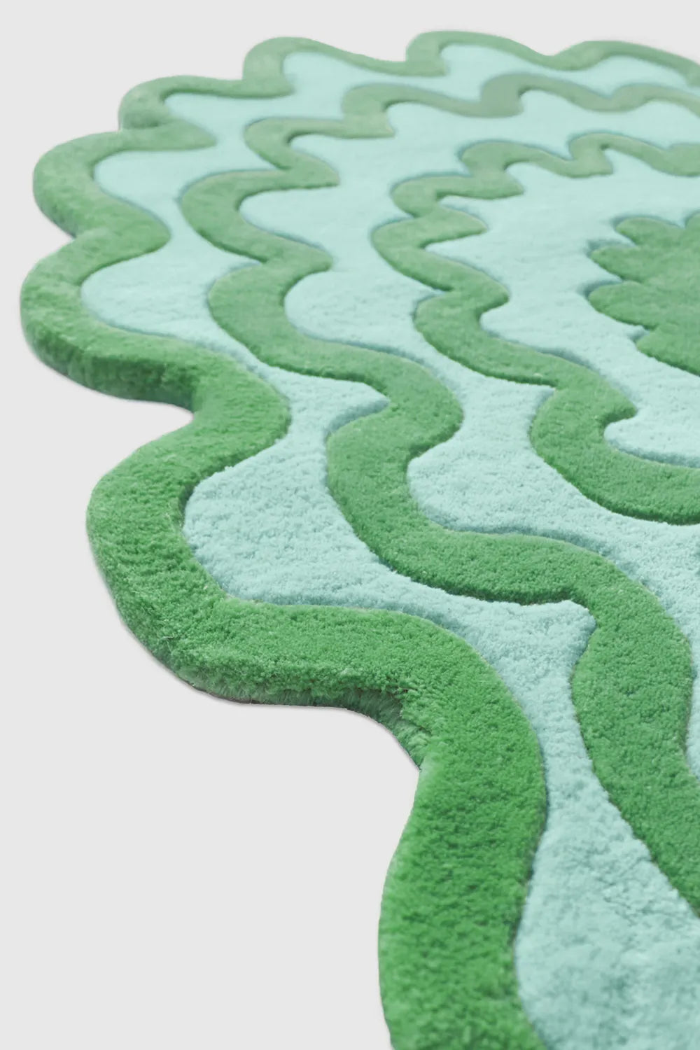 Side view of green teal and blue wavy abstract rug, highlighting sculpted tufted texture and layered organic design.