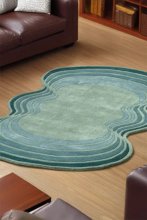 Green oval rug on a wooden floor with a brown leather sofa and wicker baskets in the background.