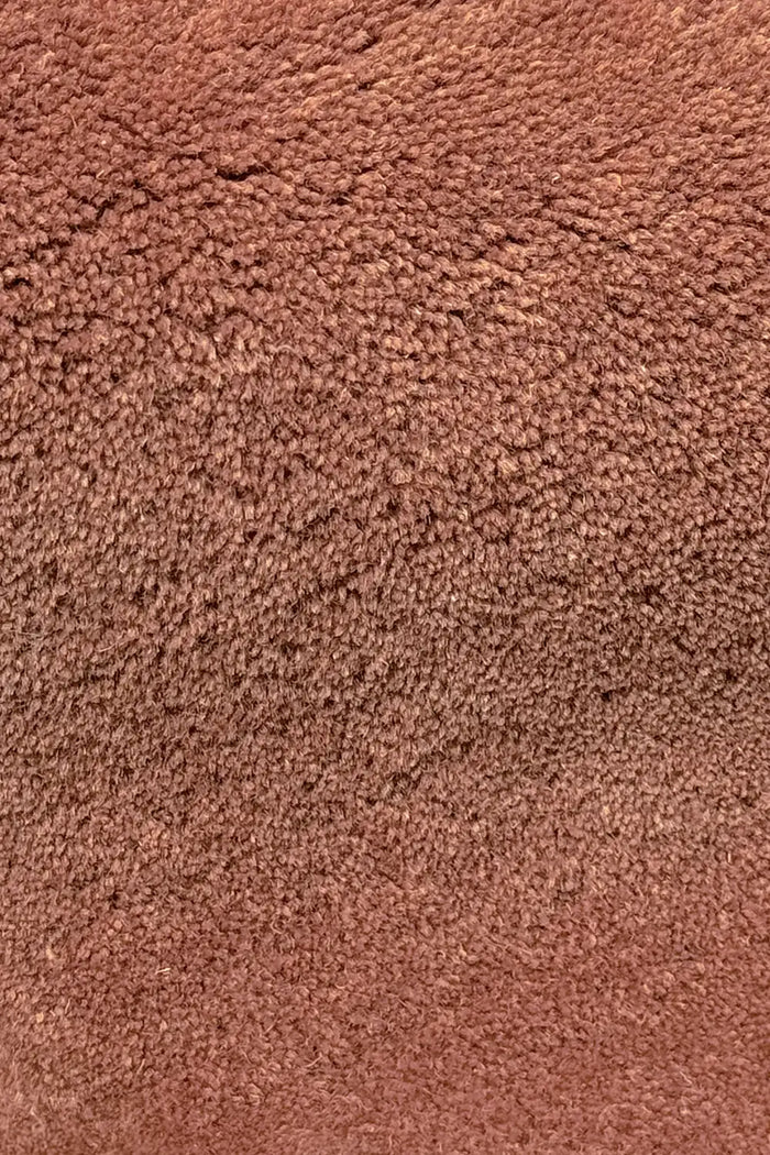 Close-up texture of plush terracotta rust wool modern rug with sculpted wavy edges in brown and burgundy