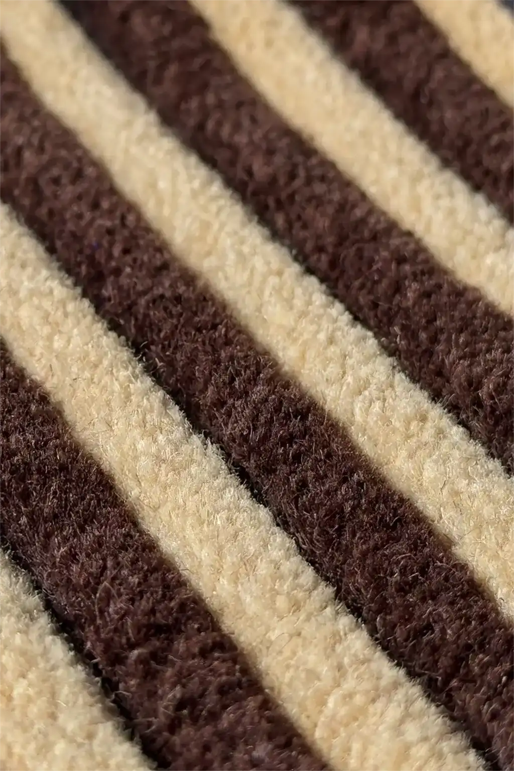 A close-up of a textured striped runner rug with alternating thick diagonal bands of dark brown and warm cream.