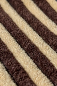 A close-up of a textured striped runner rug with alternating thick diagonal bands of dark brown and warm cream.