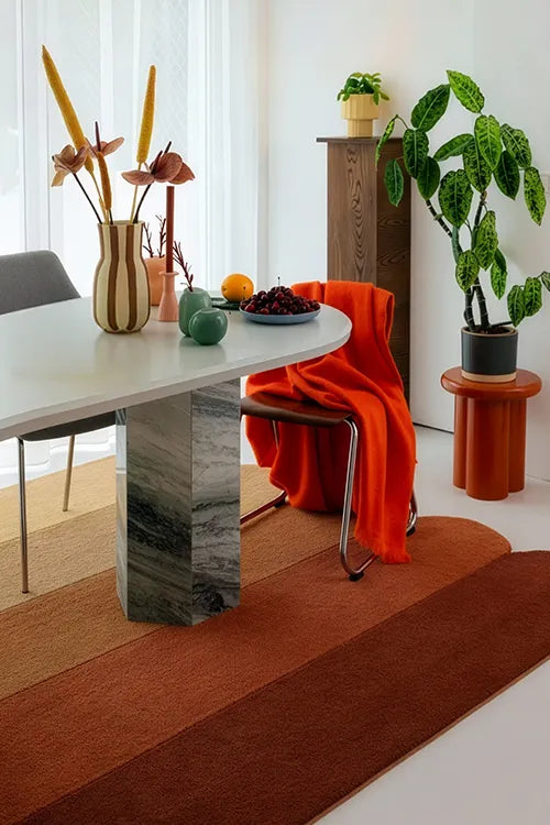 Modern dining room with unique scalloped rug, marble table, orange chair, and decorative elements.