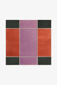 square rug with a geometric pattern of color blocks in orange, purple, and green on a white background