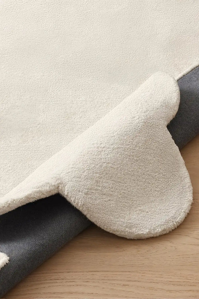 Close-up of plush cream wool rug with scalloped border, featuring soft hand-tufted pile and durable backing
