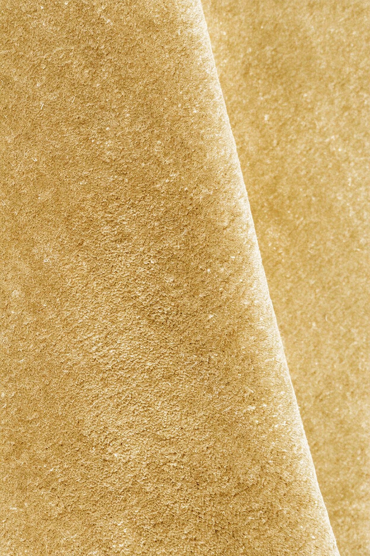 A close-up of a textured rug in a warm yellow gold color, folded diagonally to show the surface texture.