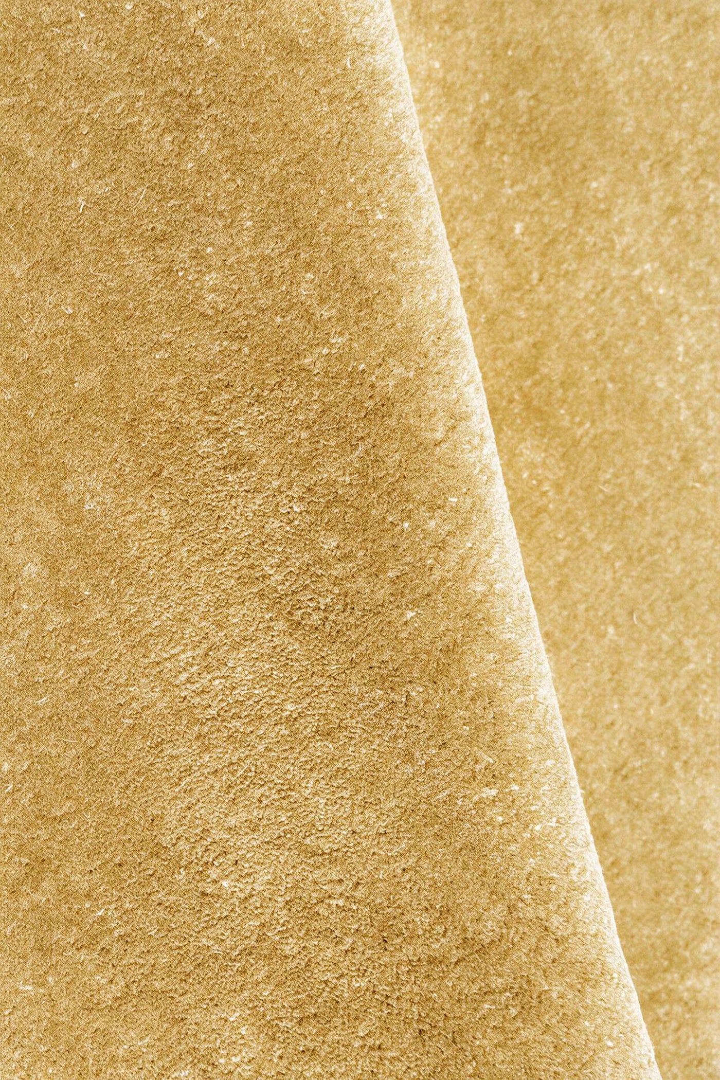 A close-up of a textured rug in a warm yellow gold color, folded diagonally to show the surface texture.