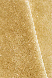 A close-up of a textured rug in a warm yellow gold color, folded diagonally to show the surface texture.