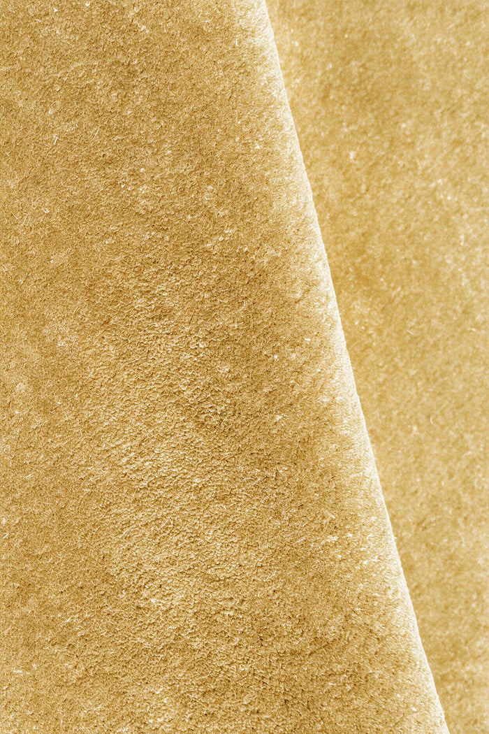 A close-up of a textured rug in a warm yellow gold color, folded diagonally to show the surface texture.
