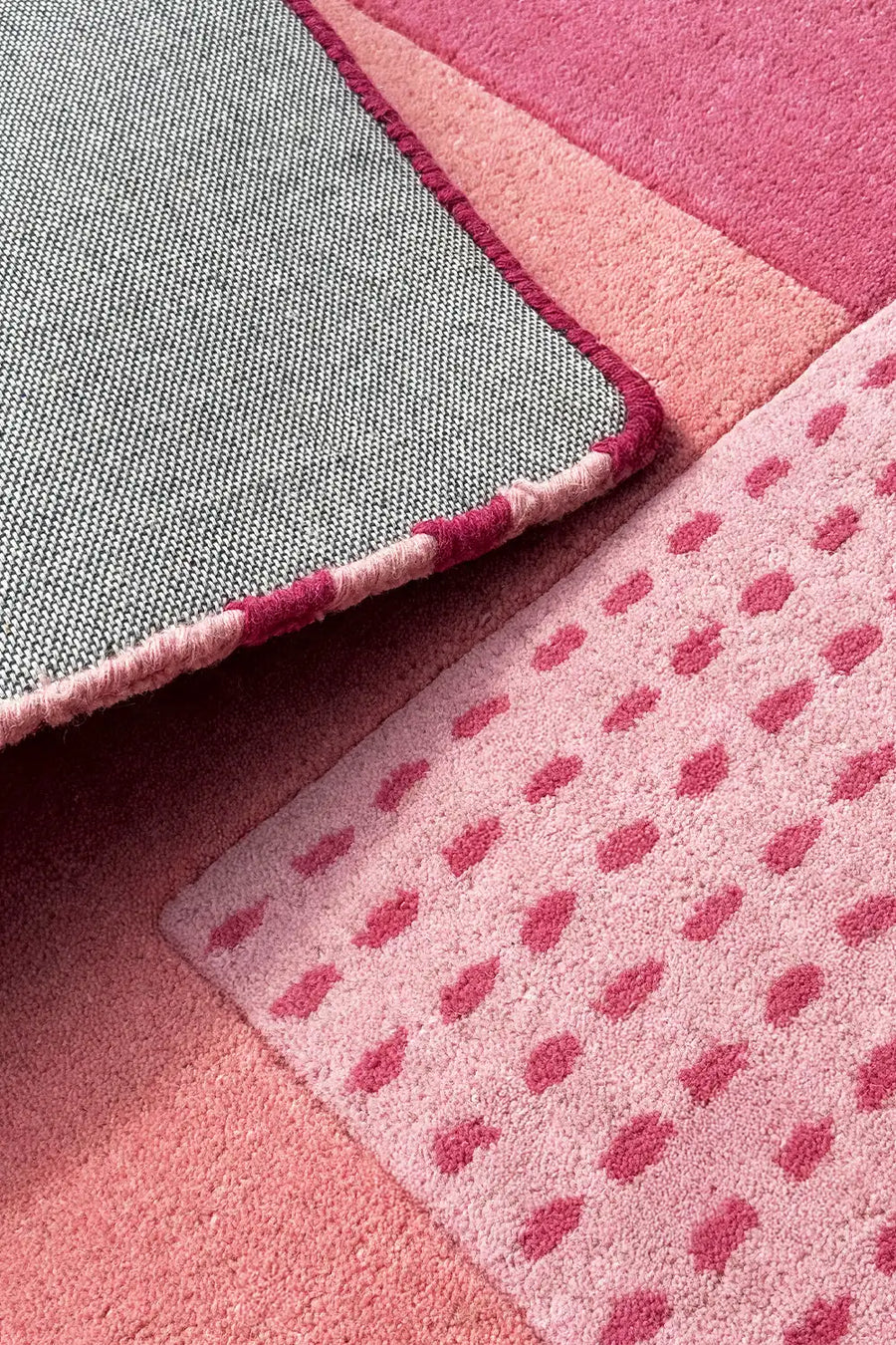 Folded corner of graphic pink wool rug showing cotton backing, hand-tufted texture, and block color detail