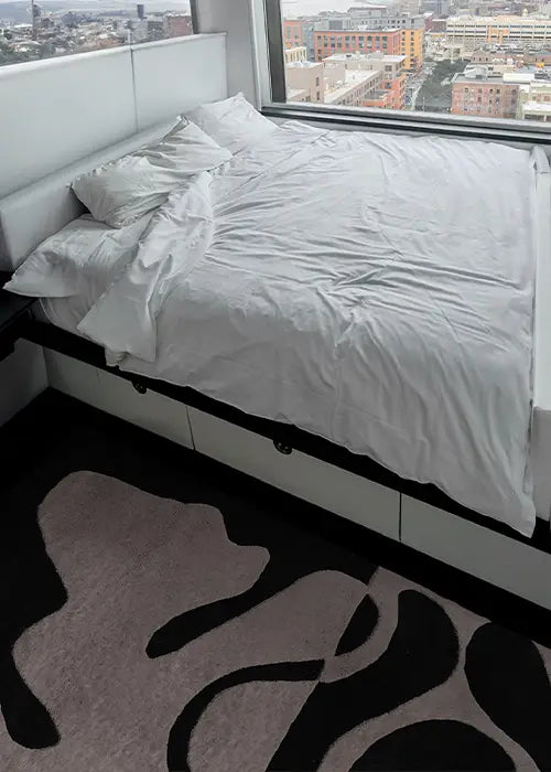 Modern abstract rug in black and white, adding contrast to a minimalist bedroom with city views.