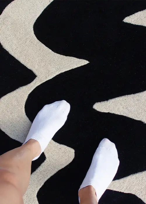 Person wearing white socks standing on a plush black and white abstract rug, highlighting its soft wool texture.