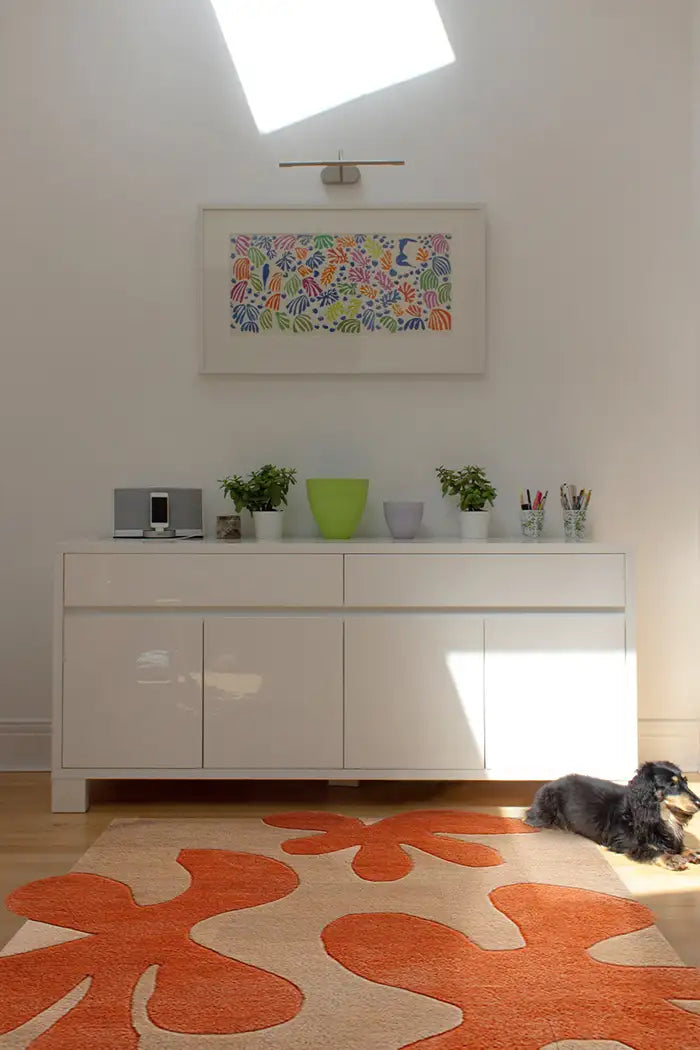 Mid-century modern floral rug in warm orange tones beneath a white credenza in a bright, airy interior with colorful wall art