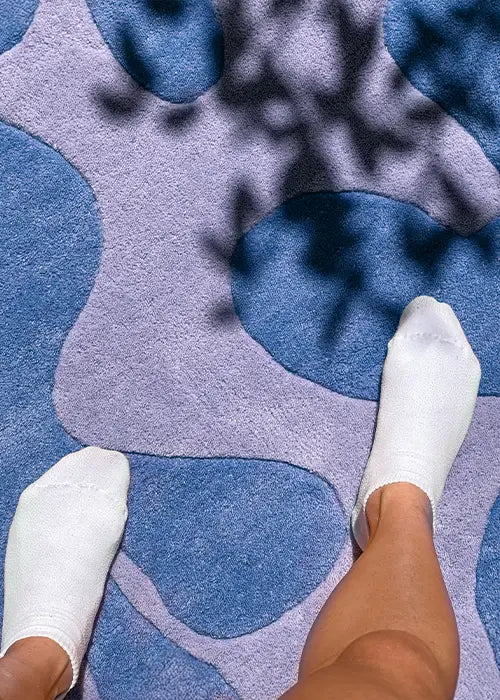 Feet on a soft blue and lavender wool rug with organic shapes, dappled in natural sunlight.