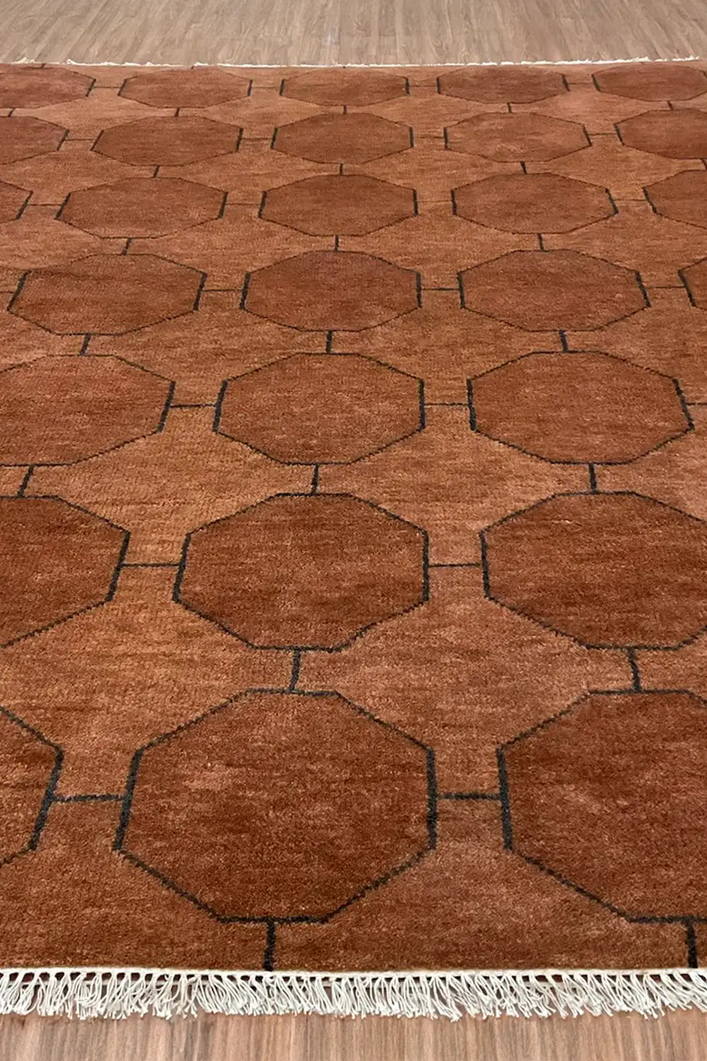 A wide shot of the brown geometric rug on a wooden floor, showcasing its full design with visible fringe edging