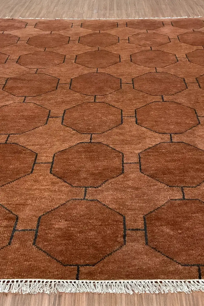 A wide shot of the brown geometric rug on a wooden floor, showcasing its full design with visible fringe edging