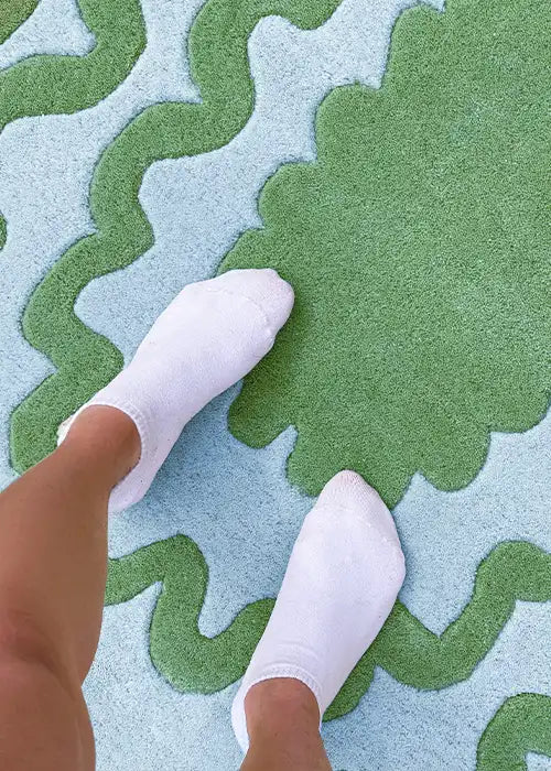 Close-up of a green and blue scalloped rug with a person’s feet in white socks