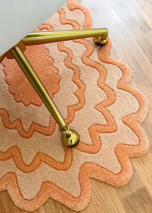 Close-up of a orange scalloped rug styled with a brass chair on a wooden floor.