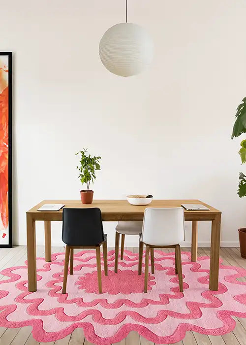 Pink scalloped rug placed under a wooden dining table with mismatched chairs in a bright room