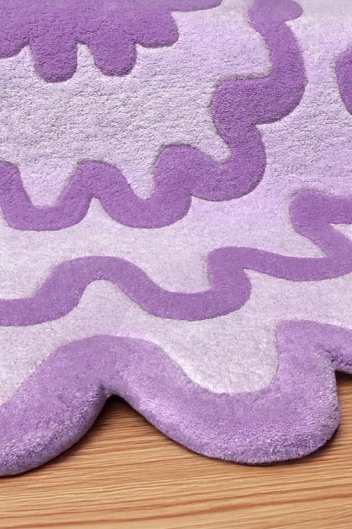 Detail of lavender and purple wavy rug with sculpted edge on wood floor.