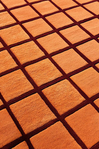 Mid century wool rug in terracotta and dark burgundy brown with raised grid design and sculpted carved pile
