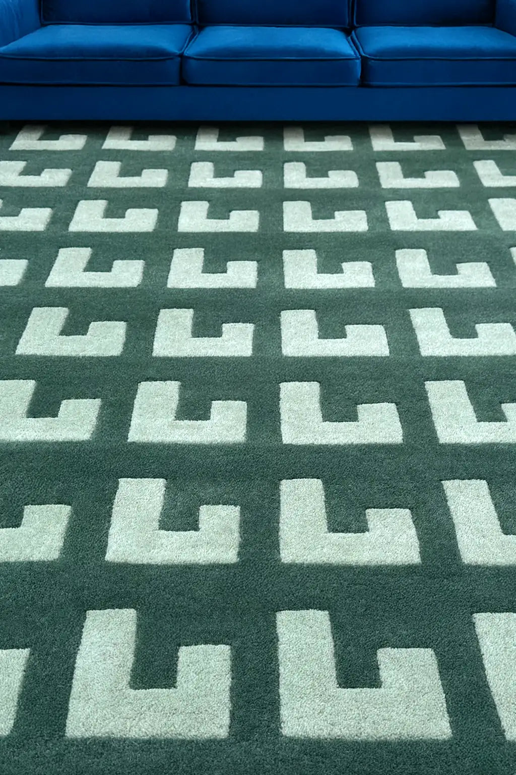 Large green geometric area rug with grid pattern styled in modern living room with deep blue sofa lifestyle