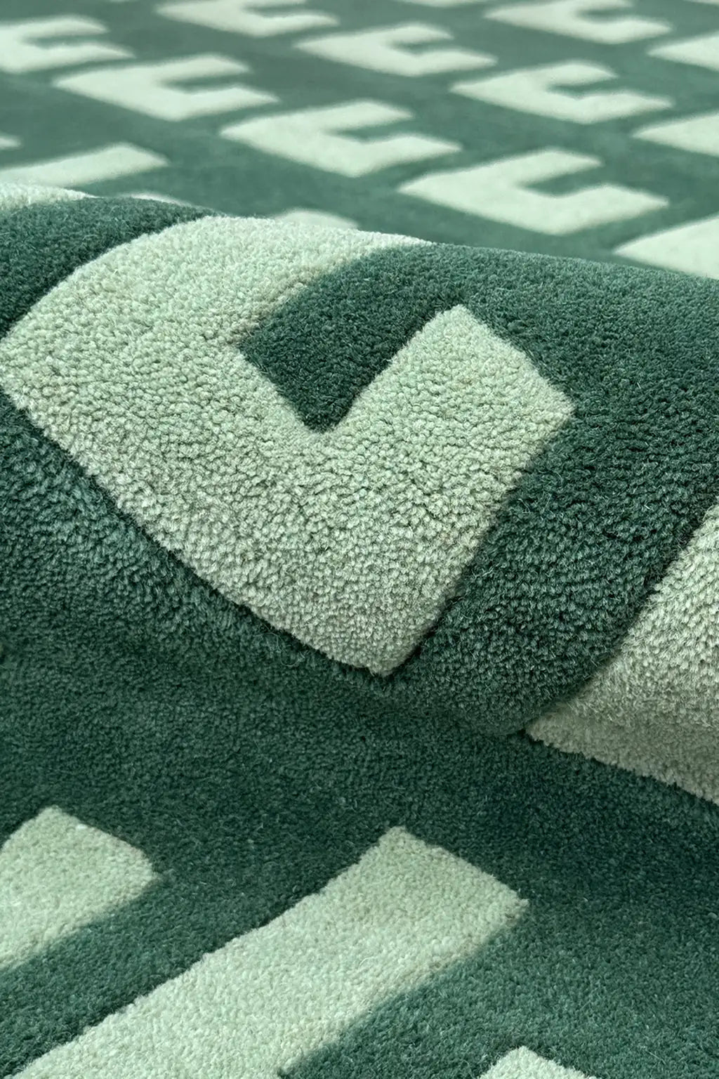 Detail of tufted wool rug in dark green with light mint block motif and sculpted texture

