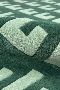 Detail of tufted wool rug in dark green with light mint block motif and sculpted texture
