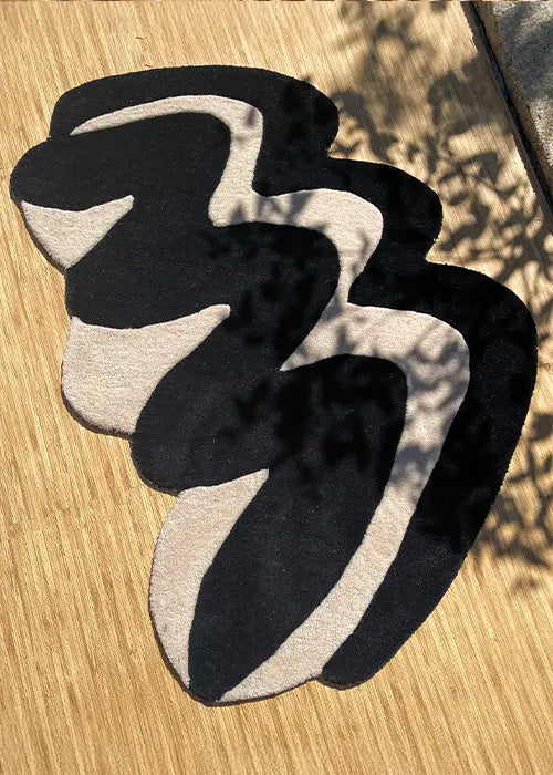 Hand-tufted black and white irregular-shaped rug in natural sunlight, emphasizing its unique, modern form