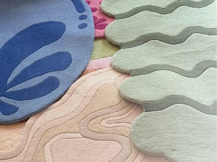 A collection of overlapping abstract-shaped wool rugs in soft blue, green, pink, and beige tones with carved detailing.
