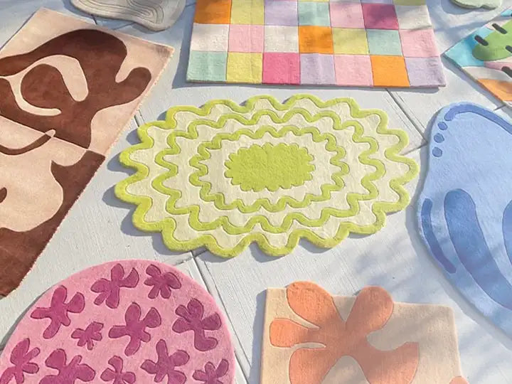 A collection of colorful, uniquely shaped rugs displayed on a light surface, featuring abstract and wavy designs in various hues including green, brown, pink, and blue.
